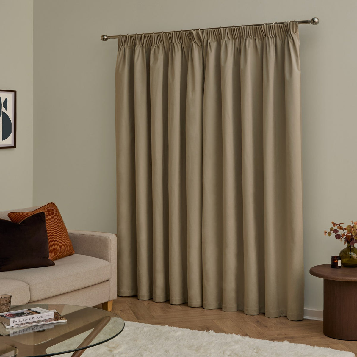 Mocha velvet pencil pleat curtains with pencil-pleat heading on a metal pole, shown covering a window in a living room with a beige sofa and wooden side table.