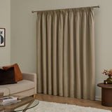Mocha velvet pencil pleat curtains with pencil-pleat heading on a metal pole, shown covering a window in a living room with a beige sofa and wooden side table.
