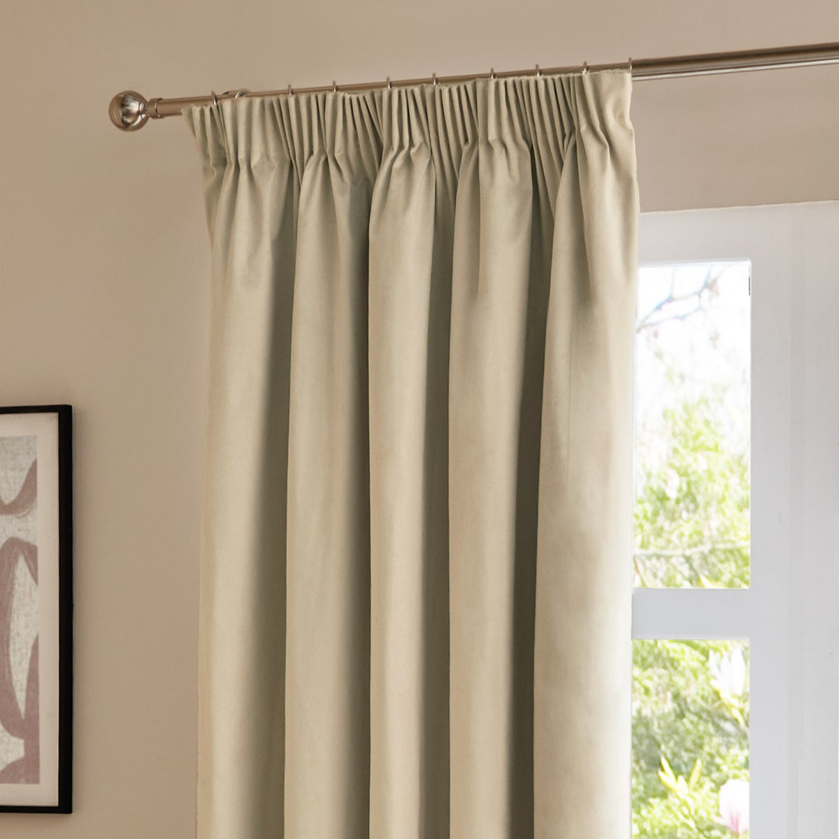 Natural velvet pencil pleat curtains with pinch-pleated heading on a chrome pole, shown in a room beside a window with sheer voile and daylight.