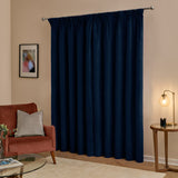 Royal blue velvet pencil pleat curtains hanging on a chrome pole in a living room, styled with a rust armchair, side table lamp, and framed wall art.