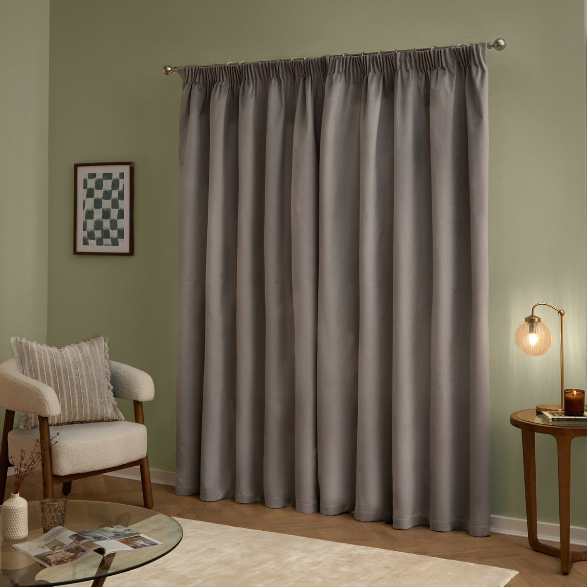 Silver-grey velvet pencil pleat curtains hung on a metal pole in a living room, shown as a full-length pair with a soft matt finish against sage green walls.