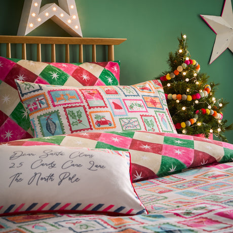 Dear Santa reversible duvet cover set on a bed with Christmas stamp print pillowcases and geometric pink and green reverse, styled with a mini tree and star lights.