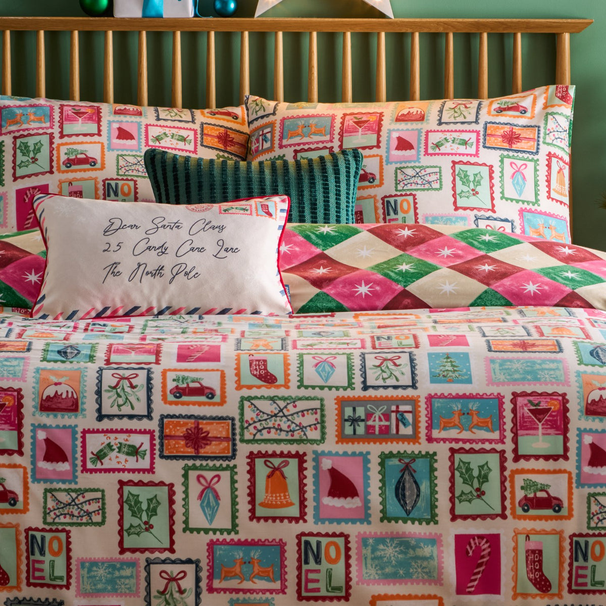 Reversible Dear Santa duvet cover set on a bed, cream side with colourful Christmas postage-stamp prints, reverse pink-and-green diamond pattern, styled with matching pillowcases and cushions.