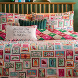 Reversible Dear Santa duvet cover set on a bed, cream side with colourful Christmas postage-stamp prints, reverse pink-and-green diamond pattern, styled with matching pillowcases and cushions.