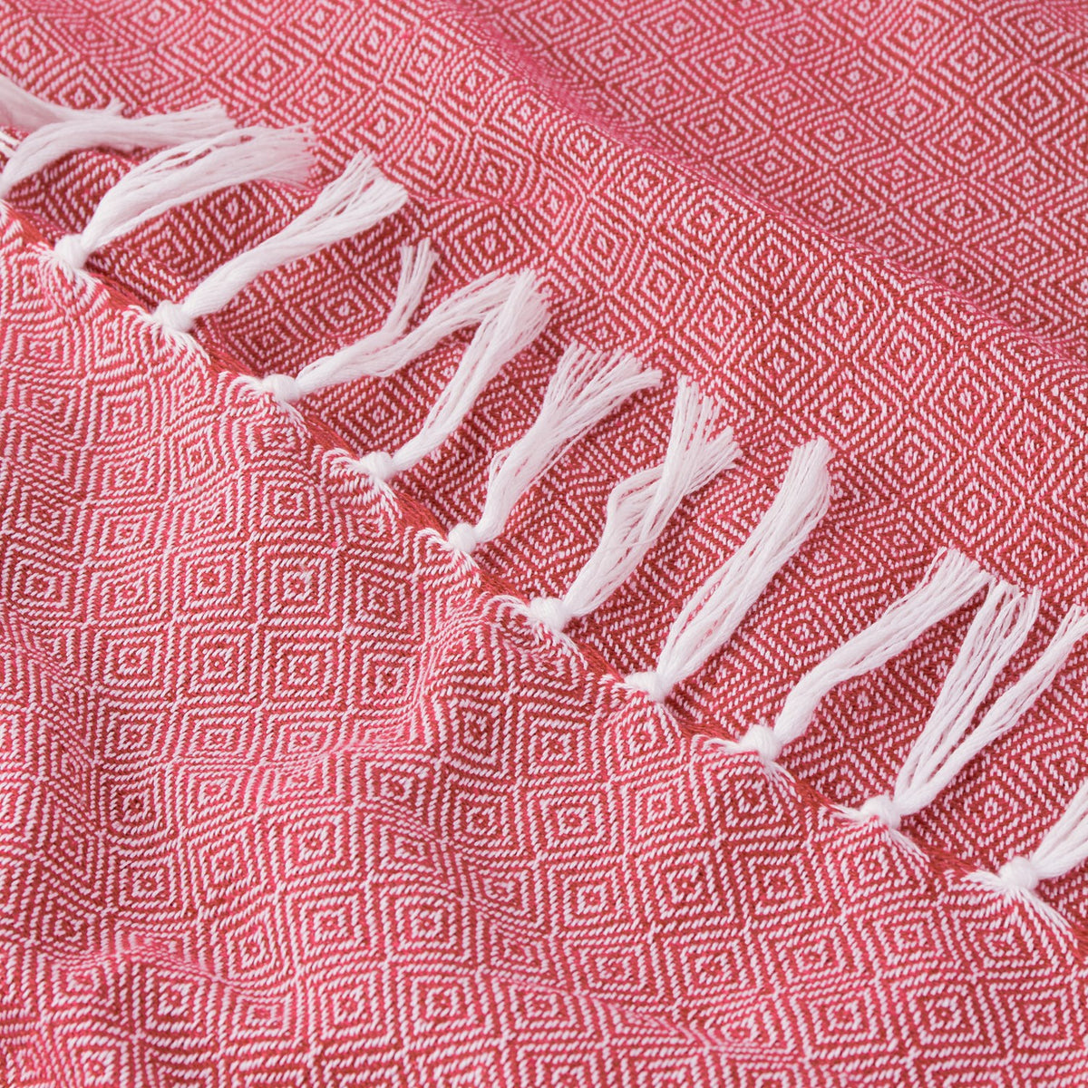 Close-up of the Dessa Geometric Polyester Throw in fuchsia, showing a woven pink-red diamond pattern with knotted off-white fringe along the edge.