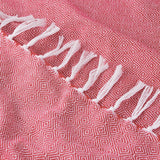 Close-up of the Dessa Geometric Polyester Throw in fuchsia, showing a woven pink-red diamond pattern with knotted off-white fringe along the edge.
