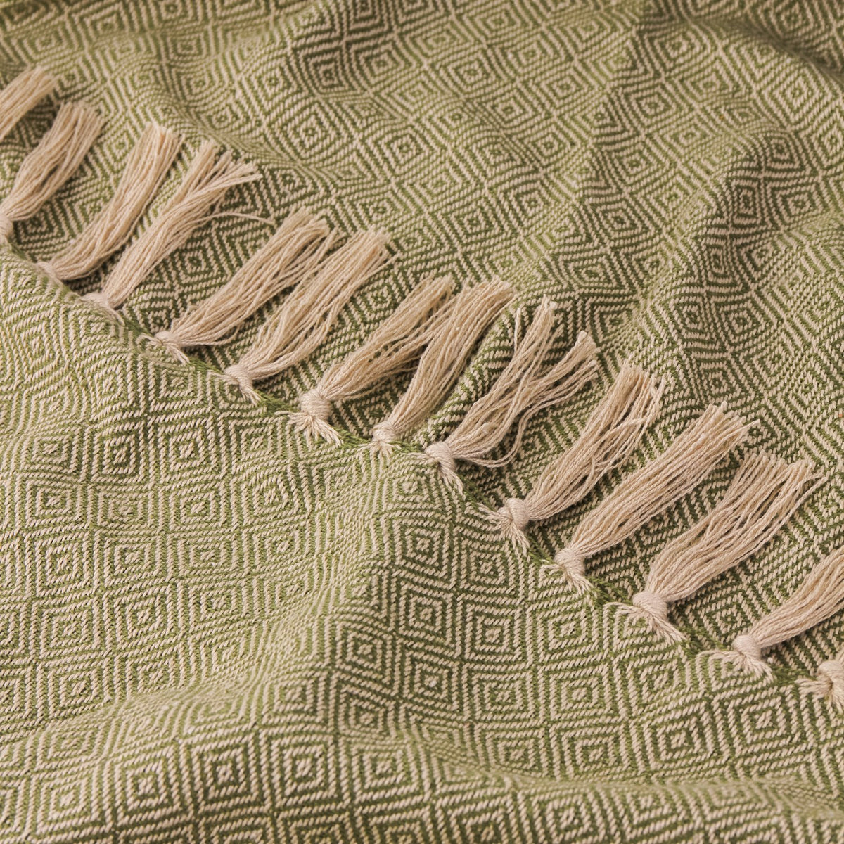 Close-up of the Dessa Geometric Polyester Throw in olive, showing the diamond lattice weave and knotted tassel fringe in a pale natural tone.