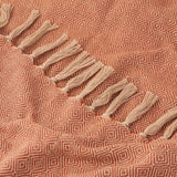 Close-up of the Dessa Geometric Polyester Throw in terracotta, showing a small diamond weave pattern with a knotted cream fringe along one edge.