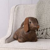 Dexter Animal Polyester Door Stop in Brown, a dachshund-shaped doorstop with mottled faux leather body and floppy tan suede ears, shown on a beige armchair.