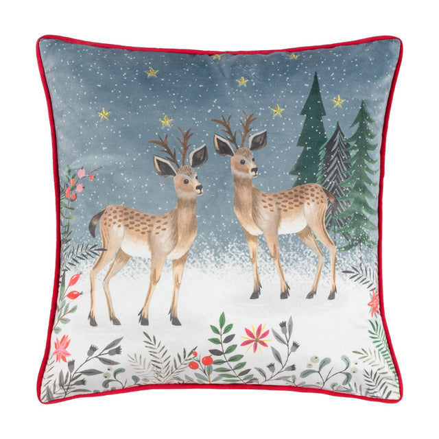 Square velvet cushion with printed reindeer and pine trees on a slate-blue snowy background, embroidered gold stars, floral border, and red piping, on a white background.