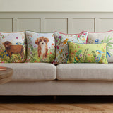 Square scatter cushion in the Daisy Hill Agnes design, printed with a Highland cow in a meadow of leaves and flowers, shown on a beige sofa among coordinating animal and bird cushions.