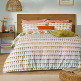Dilara Reversible Geometric Duvet Cover Set on a bed, showing the triangle-and-diamond stripe side in olive, orange, pink and blue on cream, with matching pillowcases in a bedroom setting.