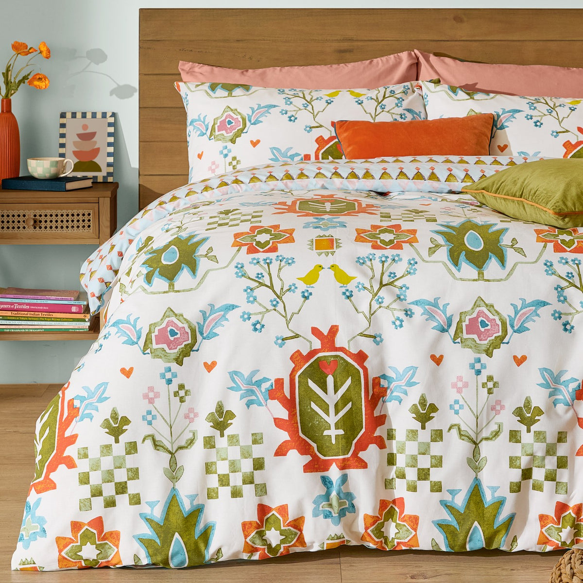 Cream cotton-blend Dilara Reversible Geometric Duvet Cover Set with folk-art bird and floral motifs in orange, olive, blue and pink, styled with matching pillowcases and accent cushions.