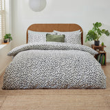 Dottie Printed Spotted Duvet Cover Set in black-on-white polycotton, styled on a bed with matching pillowcases and a green velvet cushion in a modern bedroom setting.