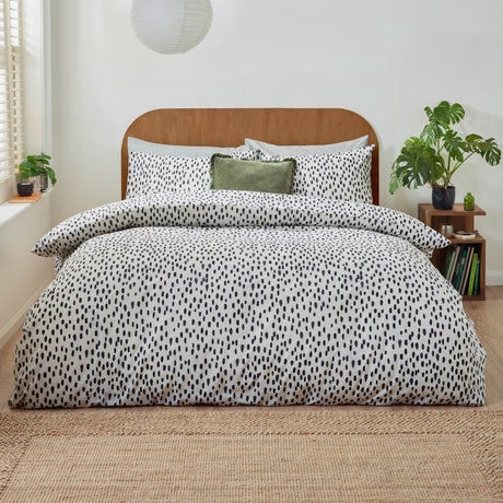 Dottie Printed Spotted Duvet Cover Set in black-on-white polycotton, styled on a bed with matching pillowcases and a green velvet cushion in a modern bedroom setting.