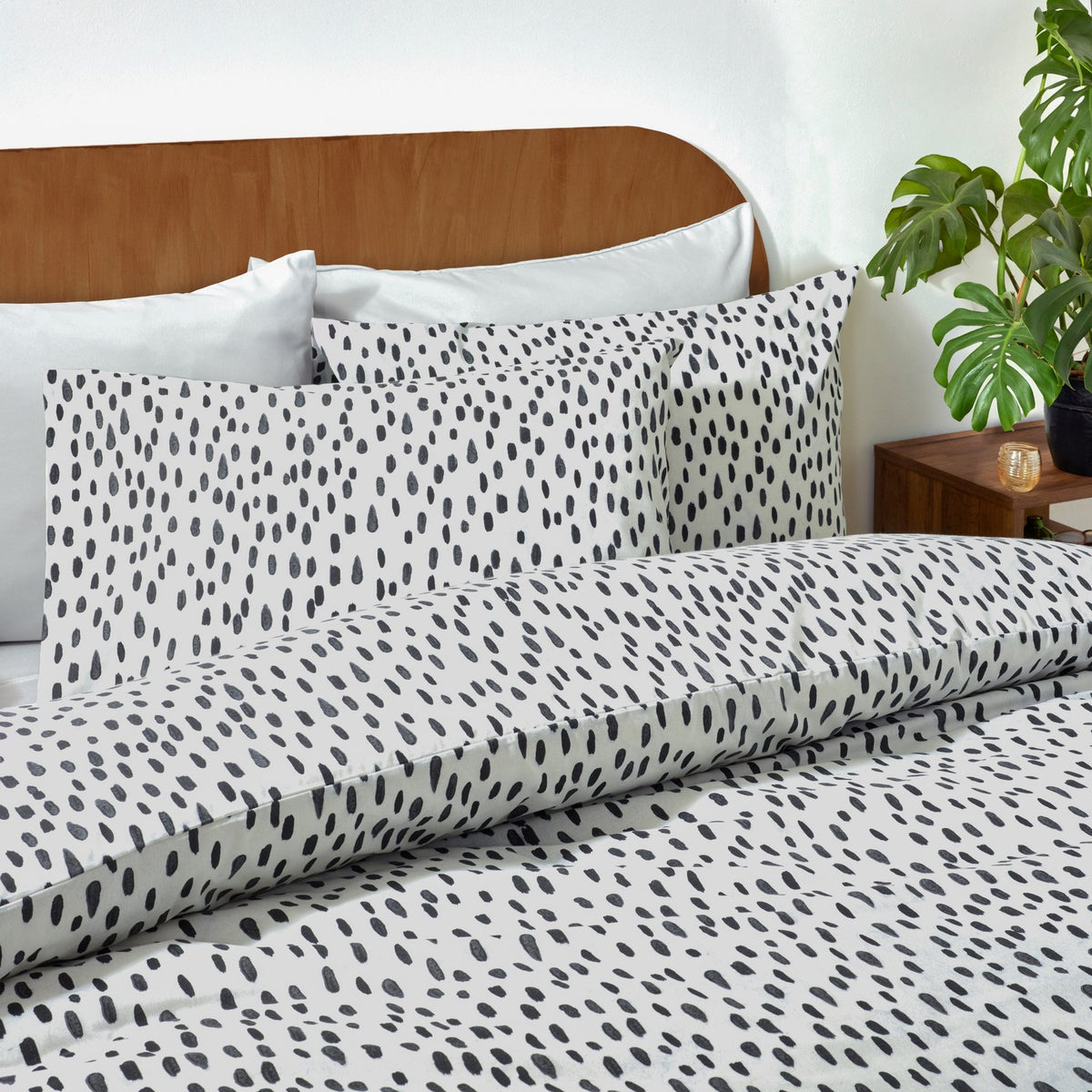 Dottie Printed Spotted Duvet Cover Set in black-on-white polycotton, shown on a bed with matching pillowcases against a wooden headboard in a bedroom setting.