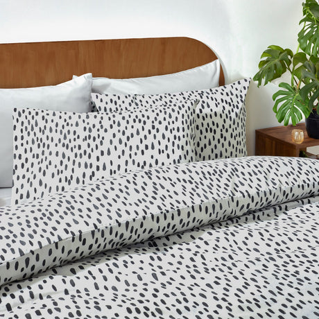 Dottie Printed Spotted Duvet Cover Set in black-on-white polycotton, shown on a bed with matching pillowcases against a wooden headboard in a bedroom setting.