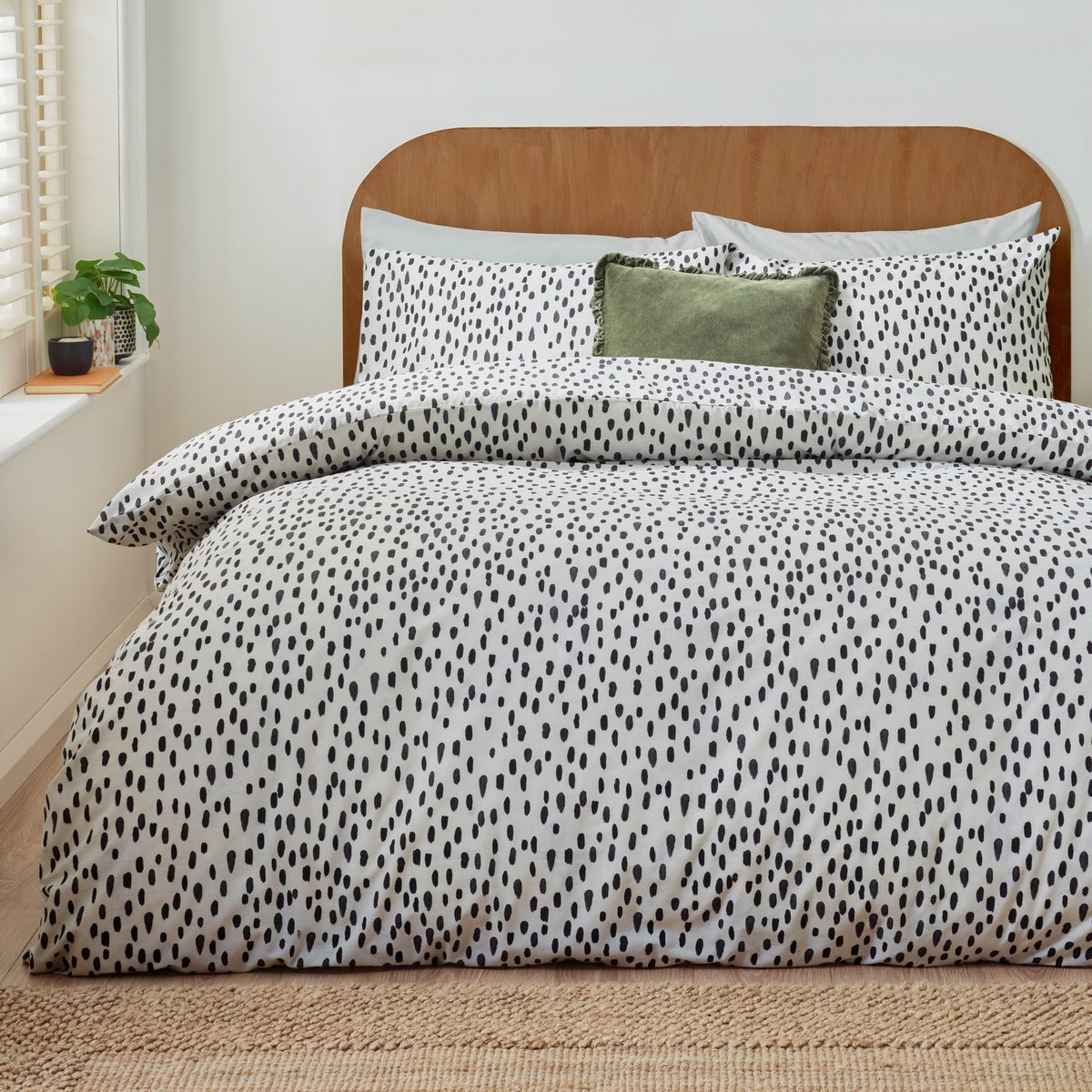 Dottie Printed Spotted Duvet Cover Set on a bed with matching pillowcases, black hand-painted spot pattern on white polycotton, styled with a green cushion in a bedroom setting.
