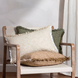 Doze Reversible Cotton Cushion in moss green with fringed edges, shown among cream and tan cushions on a wooden armchair.