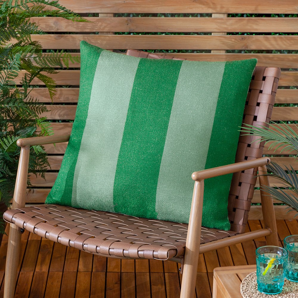 Deck Stripe reversible polyester cushion in green, broad vertical bands of bottle green and sage, shown on a woven outdoor chair against a wooden slatted backdrop.