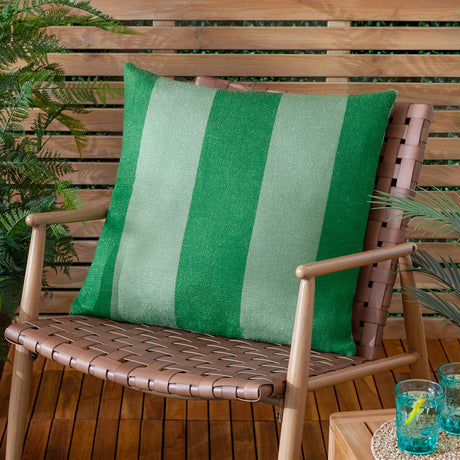Deck Stripe reversible polyester cushion in green, broad vertical bands of bottle green and sage, shown on a woven outdoor chair against a wooden slatted backdrop.