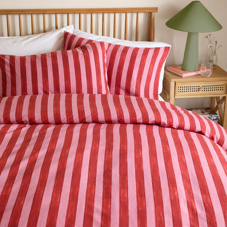 Dual Tone Printed Striped Duvet Cover Set in pink and red on a bed with matching pillowcases, wooden headboard, and green table lamp on a bedside table.