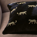 Duma Velvet Cotton Cushion in noir, a square black cotton velvet cushion embroidered with gold cheetah motifs, shown on a beige sofa.