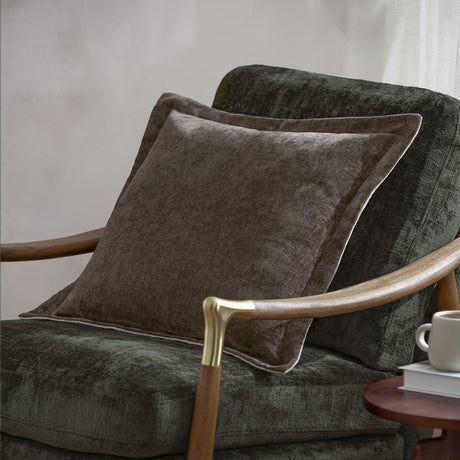 Dune Velvet Chenille Cushion in Mole, a square mid-brown chenille cushion with piped edging, shown on a dark green upholstered armchair with wooden armrests.