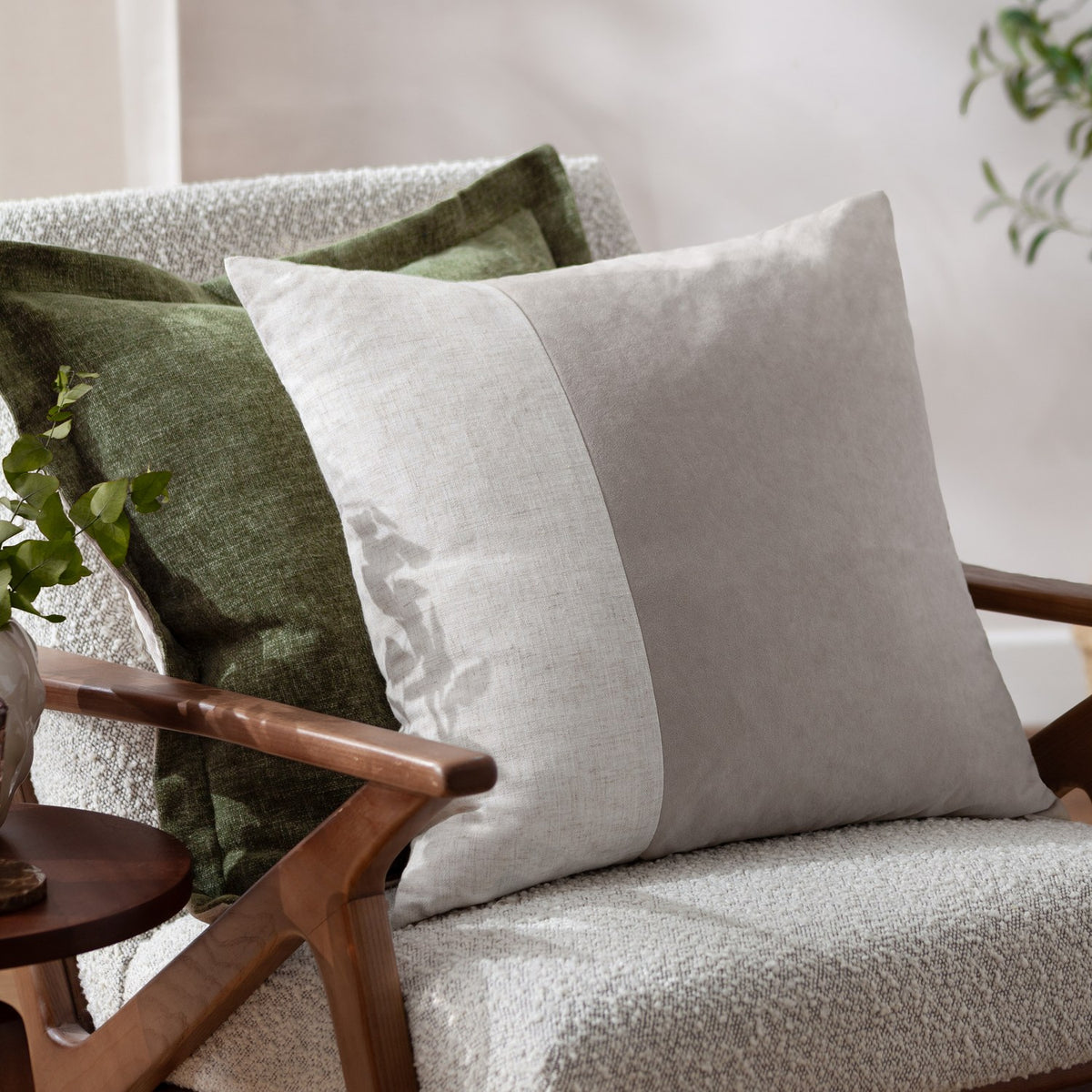 Dune Velvet Chenille Cushion in Moss green with an oxford edge, shown on a light bouclé armchair alongside a beige linen cushion.