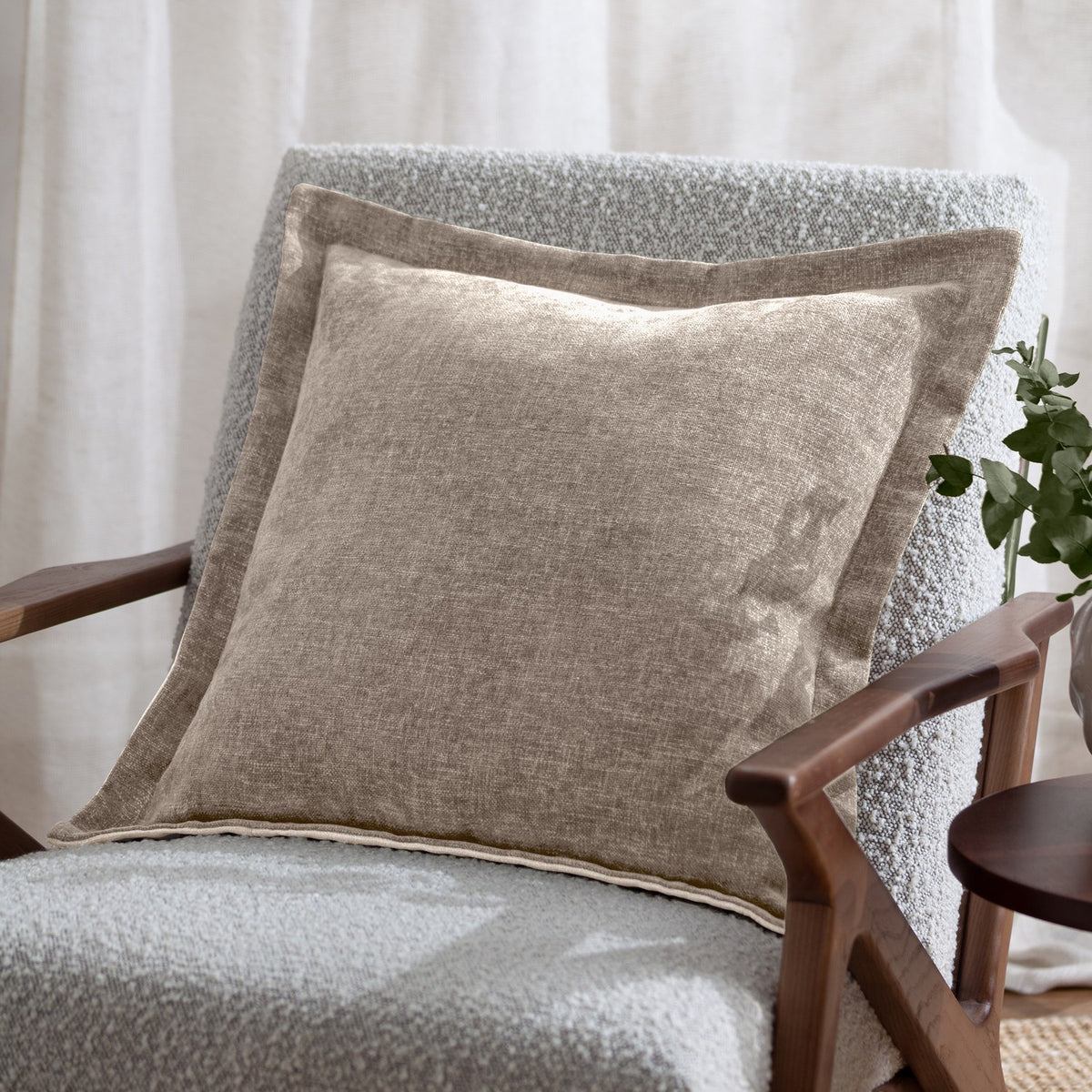 Dune Velvet Chenille Cushion in natural, square 50x50cm with a wide flat oxford border, shown on a grey boucle armchair in a living room setting.