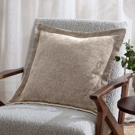 Dune Velvet Chenille Cushion in natural, square 50x50cm with a wide flat oxford border, shown on a grey boucle armchair in a living room setting.