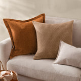 Dune Velvet Chenille Cushion in Pecan, a rust-brown square cushion with an oxford border, shown on a beige sofa alongside patterned and neutral cushions.