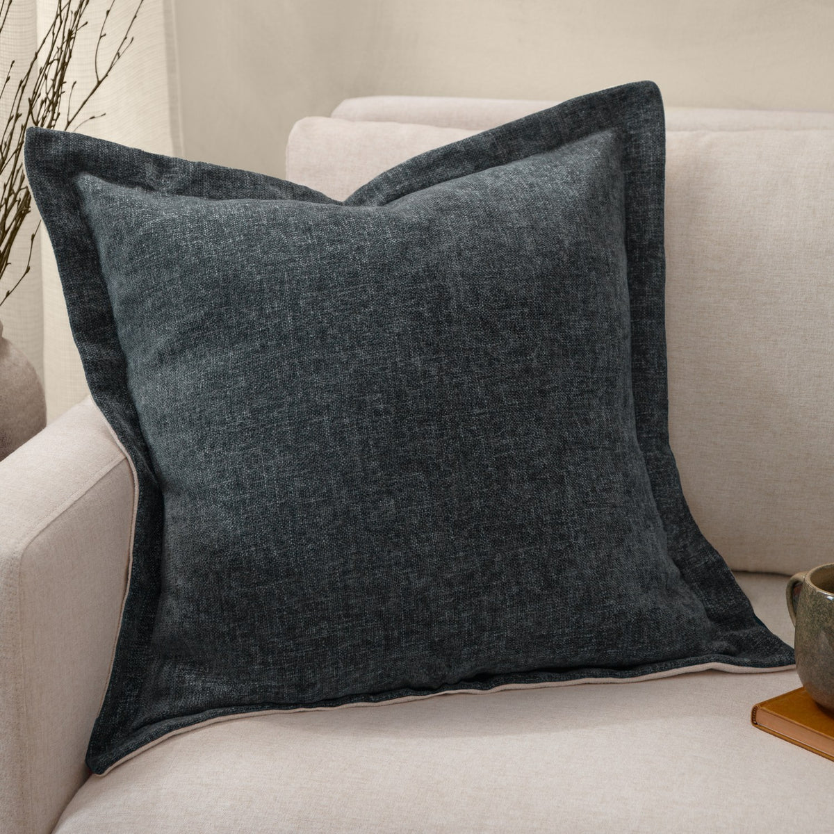 Dune Velvet Chenille Cushion in Slate, a square textured chenille cushion in deep blue-grey with flanged edge, shown on a beige sofa.