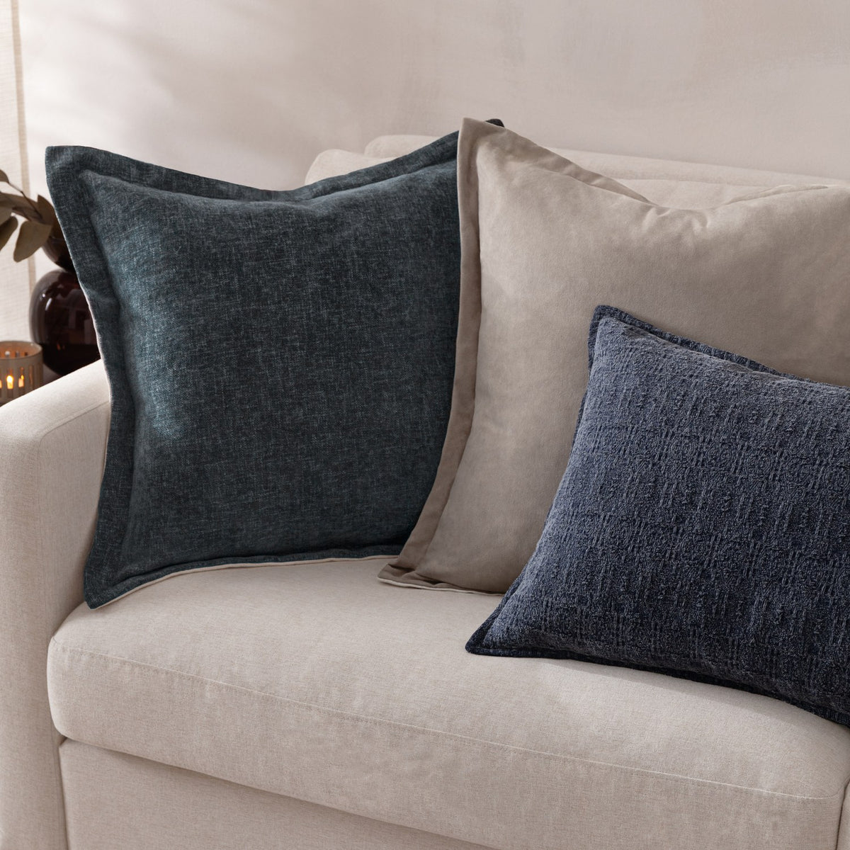 Dune Velvet Chenille Cushion in Slate blue-grey, styled on a beige sofa alongside a taupe cushion and a dark teal cushion.