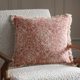 Durelle Damask Cotton Cushion in coral, a square slub cotton cushion with cream foliate damask pattern and fringed edges, shown on a bouclé armchair.