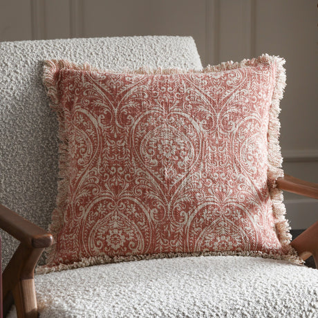 Durelle Damask Cotton Cushion in coral, a square slub cotton cushion with cream foliate damask pattern and fringed edges, shown on a bouclé armchair.