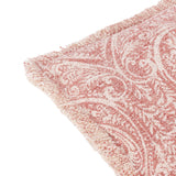 Durelle Damask Cotton Cushion in coral, close-up of the frayed edge and scrolling foliate pattern in coral-pink on a cream slub cotton ground, shown on a white background.