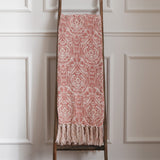 Durelle Damask Cotton Throw in coral pink and cream paisley pattern with knotted tassel fringe, draped over a wooden ladder against a panelled wall.