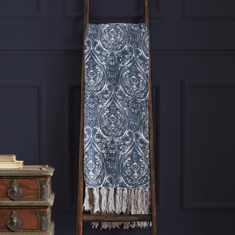 Durelle Damask Cotton Throw in Delph Blue with ivory scrolling pattern and fringed edge, draped over a wooden ladder against a dark panelled wall.