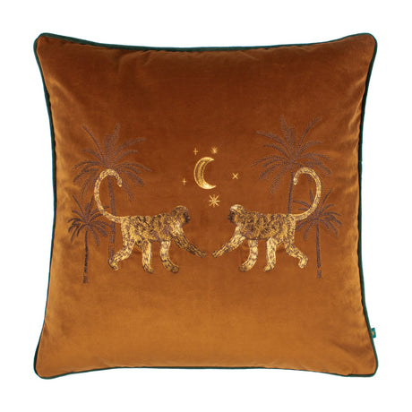 Dusk Animal Velvet Cushion in rust-orange velvet with embroidered facing monkeys, palm trees, crescent moon and stars in gold and brown thread, green piped edge, on a white background.