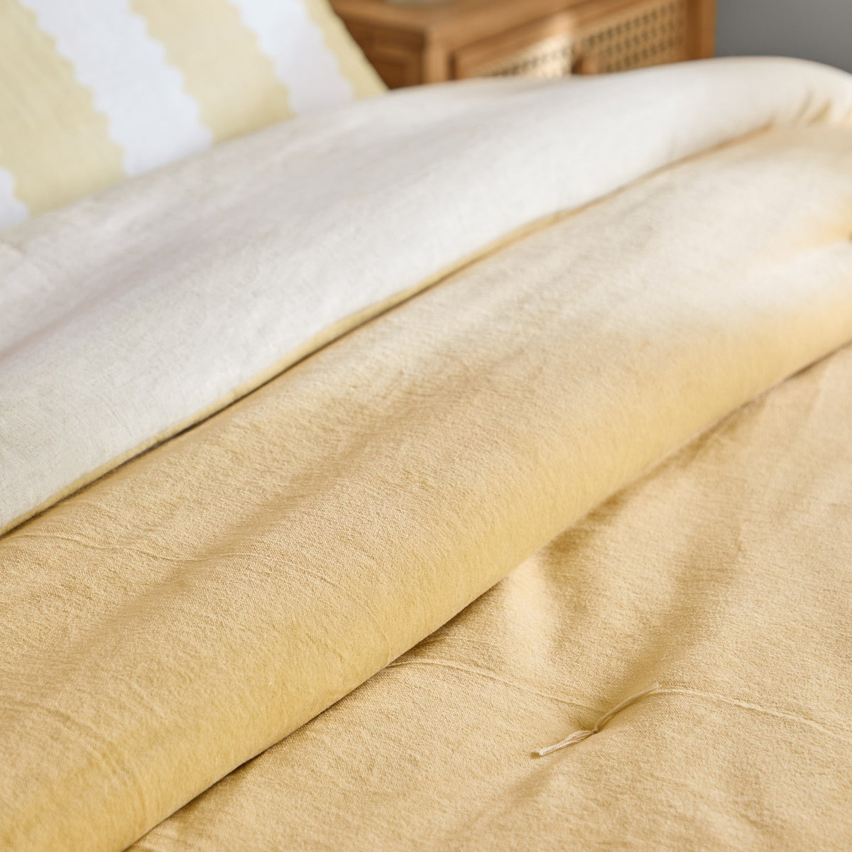 Edie Linen Cotton Bedspread in butter yellow, quilted cotton velvet folded back to reveal the paler natural linen-look reverse, shown on a bed with a tufted button detail.