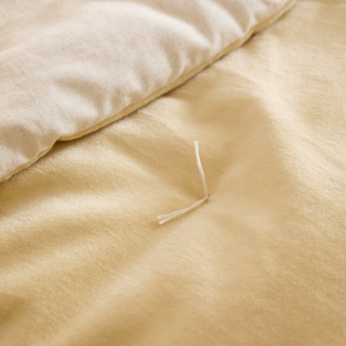 Close-up of the Edie quilted bedspread showing the butter yellow cotton velvet top folded back to reveal the paler natural linen-look reverse side.