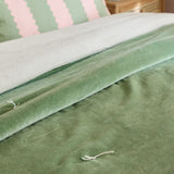 Edie Linen Cotton Bedspread in green, quilted velvet face folded back to reveal the paler linen-look cotton reverse, with a hand-tied thread detail visible on the bed.