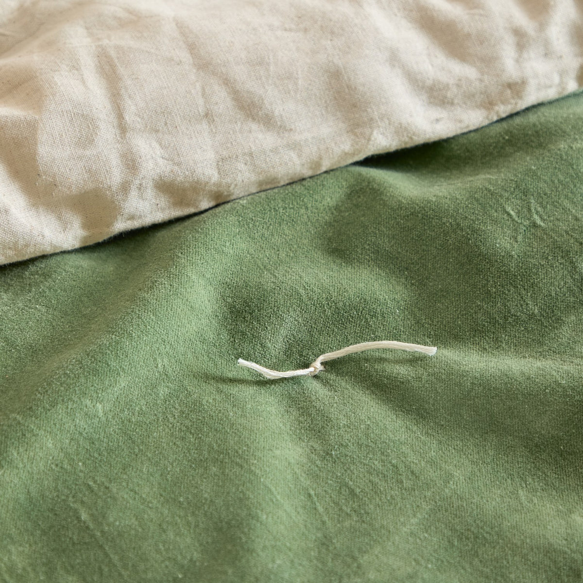 Close-up of the Edie bedspread showing the green cotton velvet face with a hand-tied thread detail, folded back to reveal the paler linen-look cotton reverse.