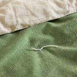 Close-up of the Edie bedspread showing the green cotton velvet face with a hand-tied thread detail, folded back to reveal the paler linen-look cotton reverse.