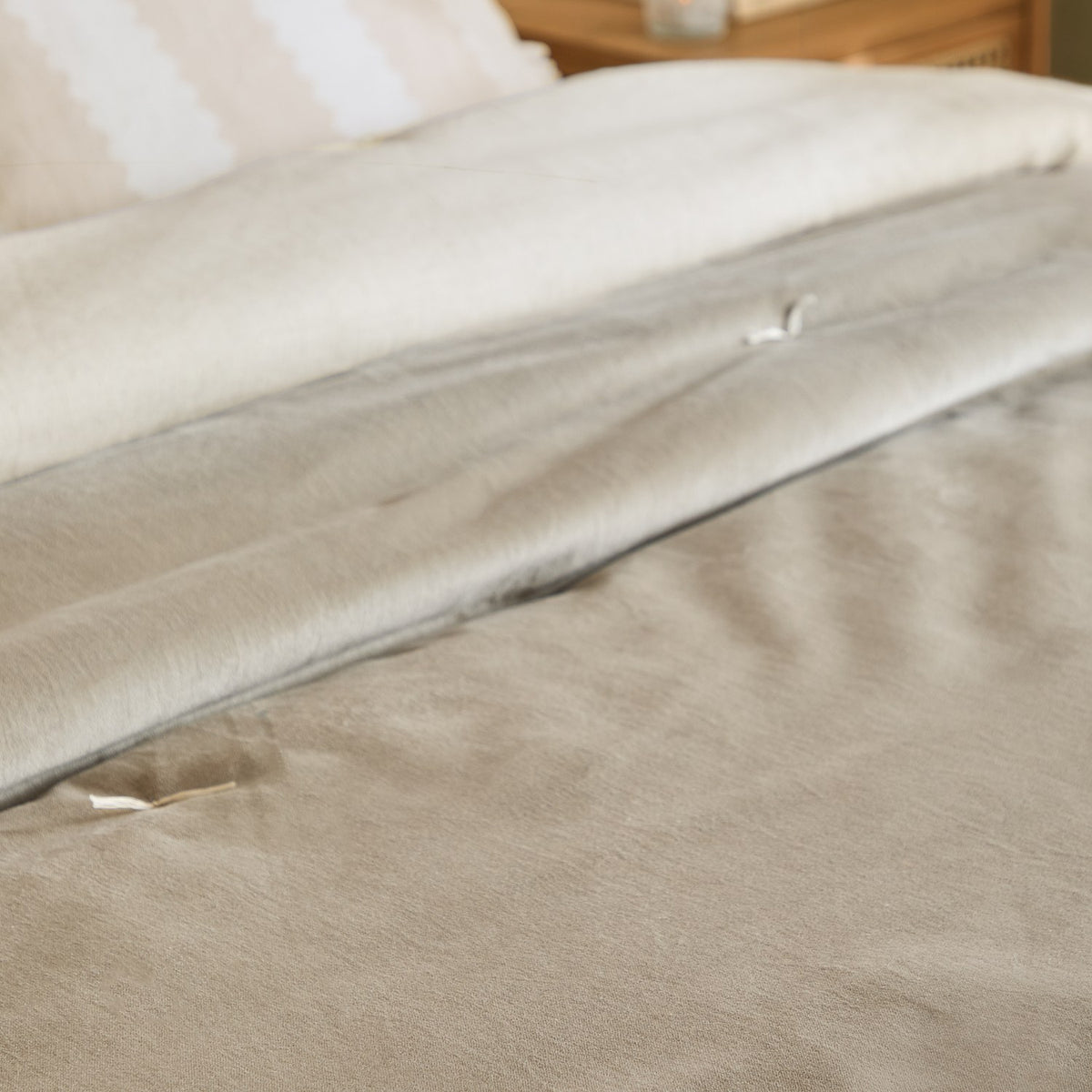 Edie Linen Cotton Bedspread in Natural, folded on a bed showing the soft velvet face and linen-look cotton reverse, styled with white and beige pillows.