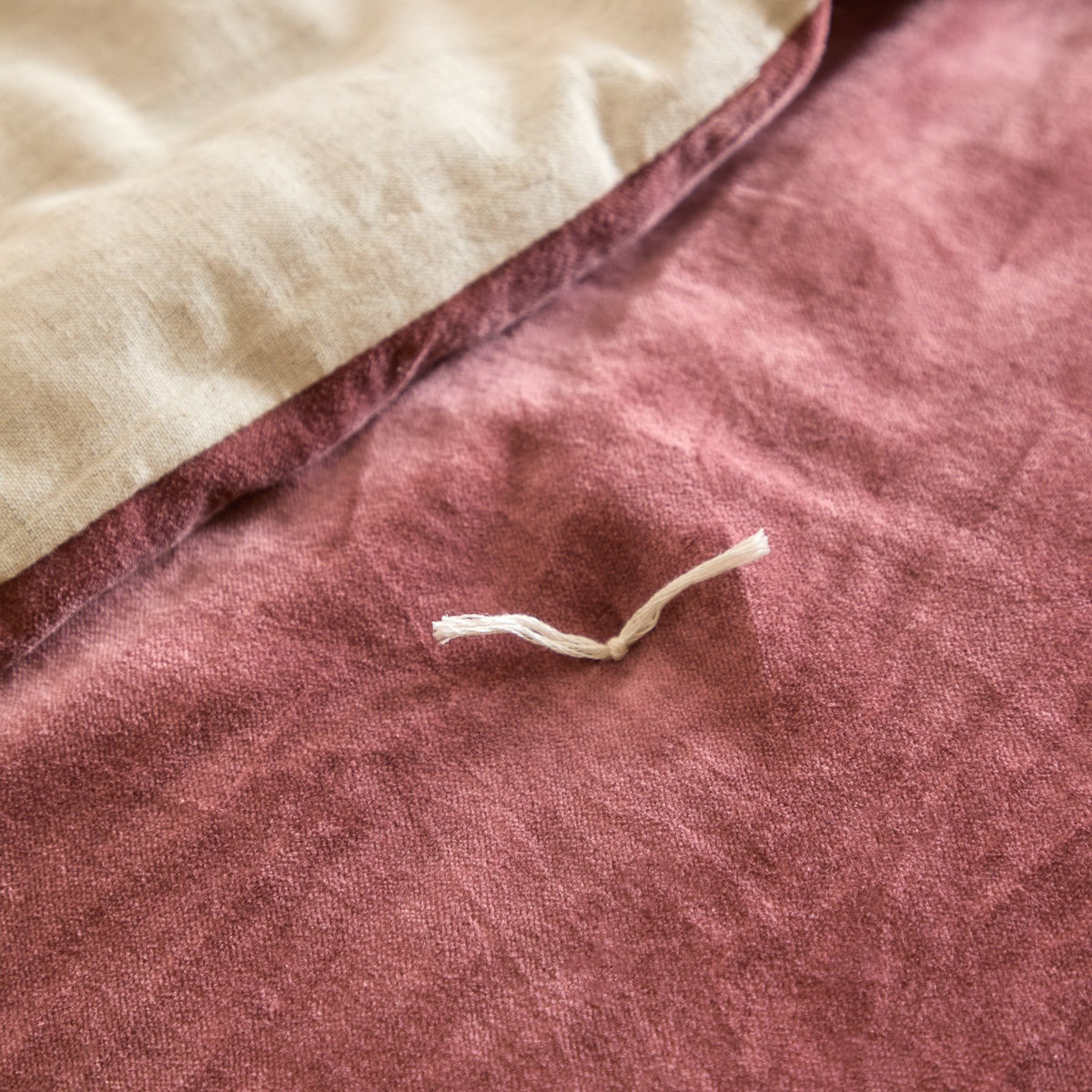 Close-up of the Edie Linen Cotton Bedspread in rose pink cotton velvet, showing the quilted surface with a hand-tied stitch and folded reverse in natural linen.