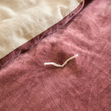 Close-up of the Edie Linen Cotton Bedspread in rose pink cotton velvet, showing the quilted surface with a hand-tied stitch and folded reverse in natural linen.