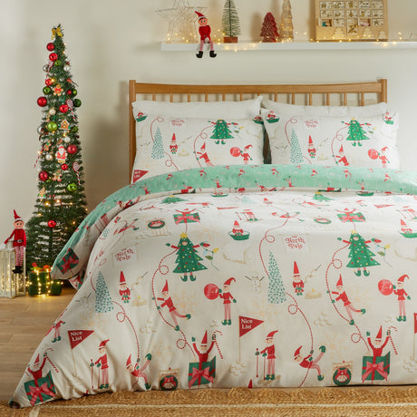 Elfie Printed Reversible Duvet Cover Set in cream and mint, dressed on a wooden bed with elf, Christmas tree, snowman and gift motifs, styled in a bedroom beside a decorated tree.