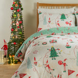 Elfie Printed Reversible Duvet Cover Set in cream, showing red-and-white elves, Christmas trees and "Nice List" flags, styled on a bed beside a decorated tree.